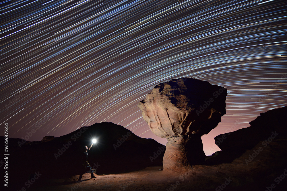 man standing near a rock mushroom and lighting it during the night with startrails in the back ground in Timna park near Eilat - Israel  - obrazy, fototapety, plakaty 