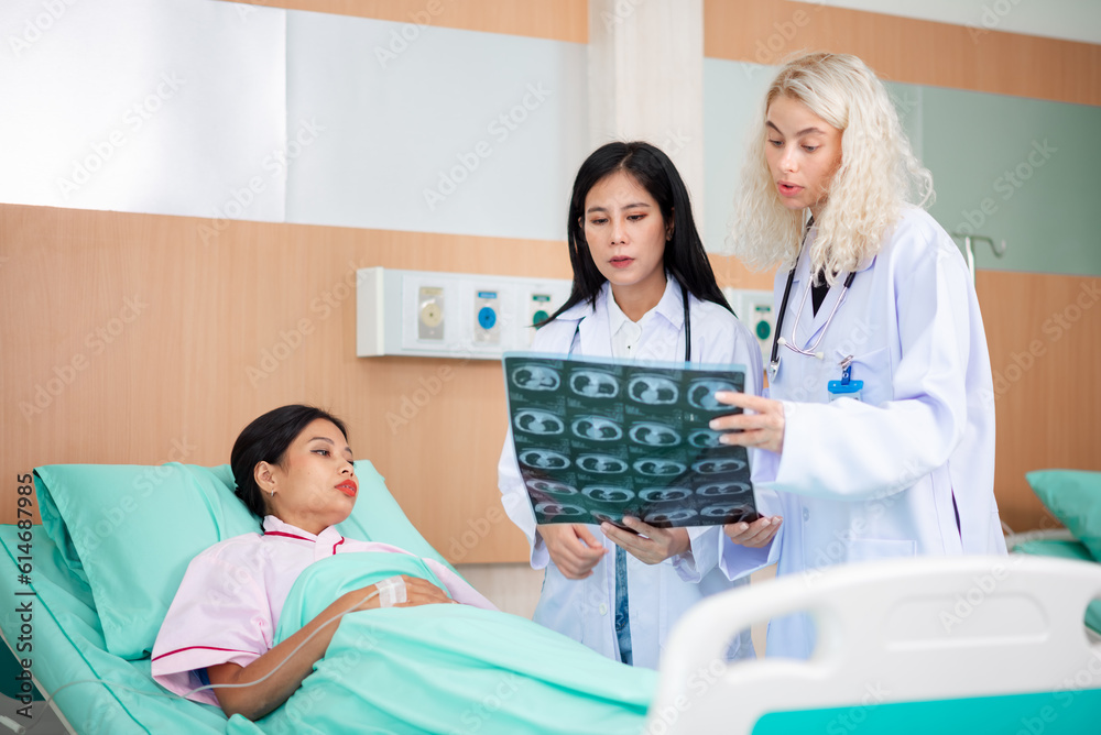 Fototapeta premium Caucasian female doctor and an Asian female doctor work together in the patient recovery room, discussing patient treatment approaches within the hospital.