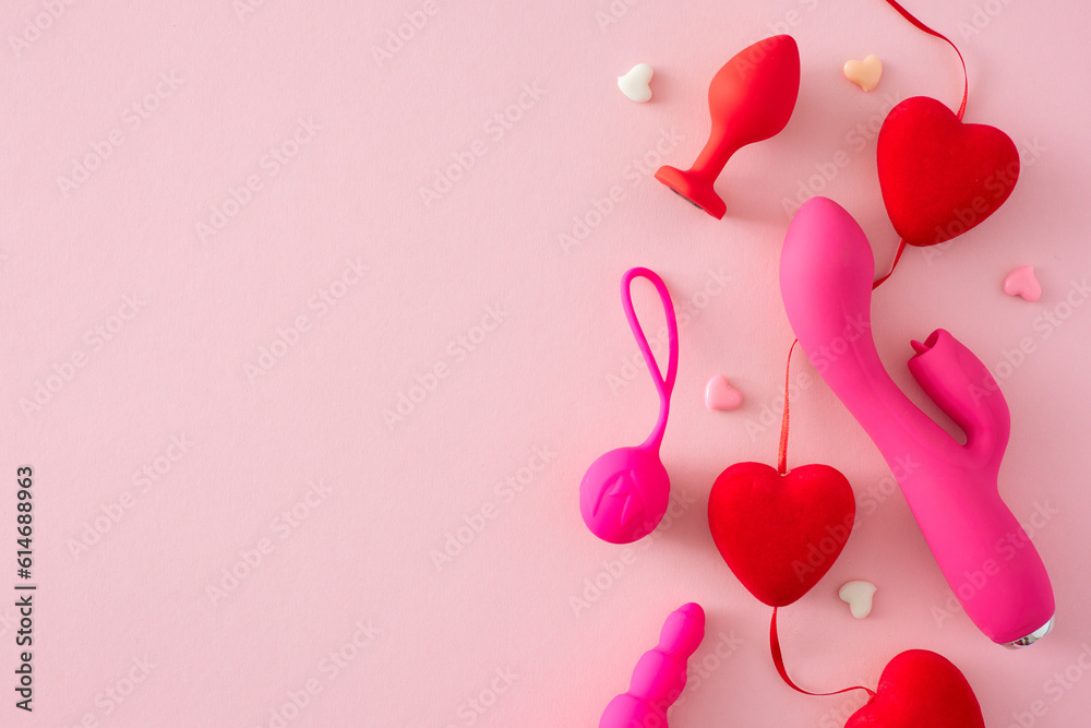 Erotic enjoyment toy ideas. Top view flat lay of pink dual vibrator, vaginal balls and anal plug and red hearts on pastel pink background with blank space for text or promo