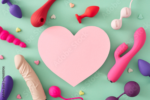 Erotic pleasure toy concepts for adults. Top view flat lay of colorful vibrators, dildo, anal plugs, vaginal balls, little hearts on turquoise background with blank heart for text or promo
