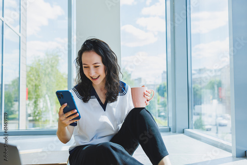 Smiling curly-haired woman sitting in a loft cafe, working at a computer, reading messages on a smartphone. Remote work Free Download Smiling curly-haired woman sitting in a loft cafe, working at a computer, reading messages on a smartphone. Remote work - GFXLoad