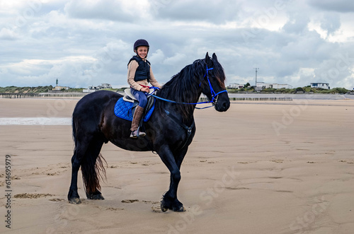 Young horsewoman with her Friesian on the beach in northern France 