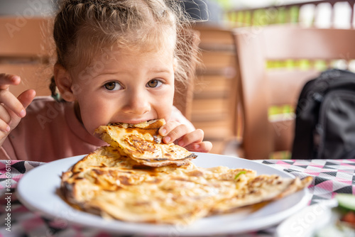 Little girl eating potato and cheese gozleme on wooden table. Traditional stuffed pancakes in Alanya  Turkey