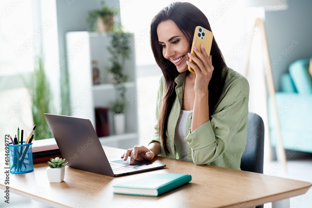 Photo of positive attractive corporate girl sit chair use wireless netbook speak communicate telephone workstation indoors Photo of positive attractive corporate girl sit chair use wireless netbook speak communicate telephone workstation indoors