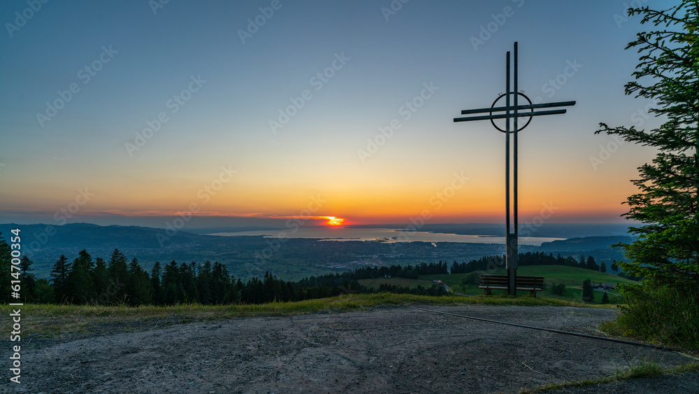 Obraz premium farbiger Sonnenuntergang über dem Bodensee, mit einem Kreuz und Sitzbank im Vordergrund