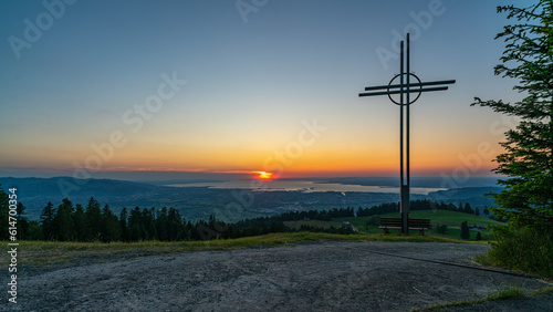 farbiger Sonnenuntergang über dem Bodensee, mit einem Kreuz und Sitzbank im Vordergrund