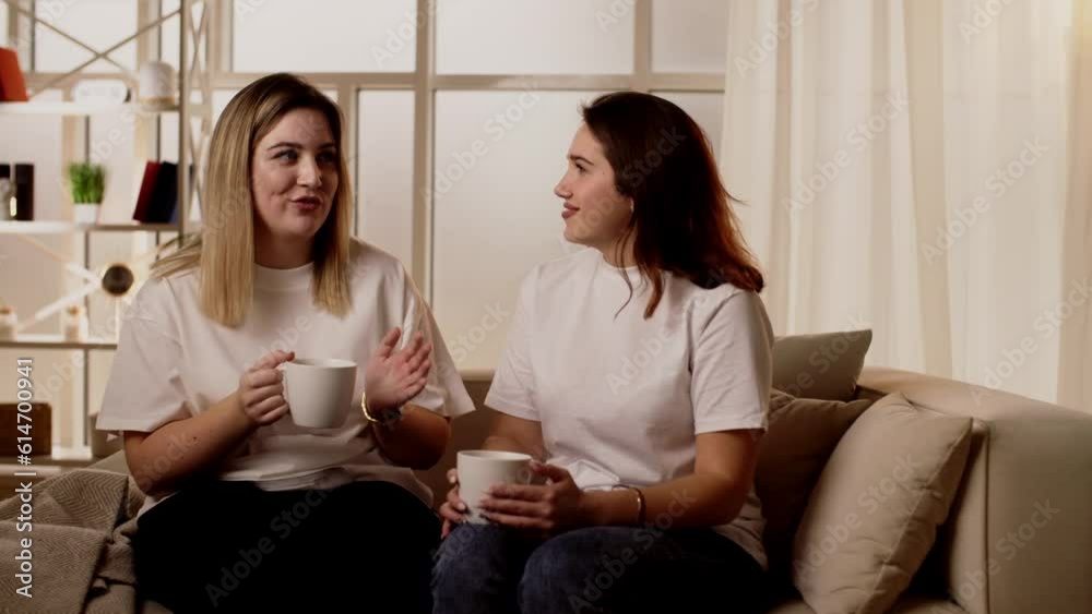 Young girls chatting about funny things, gossip laughing on the couch in the apartment. Young girls chatting about funny things, gossip laughing on the couch in the apartment.
