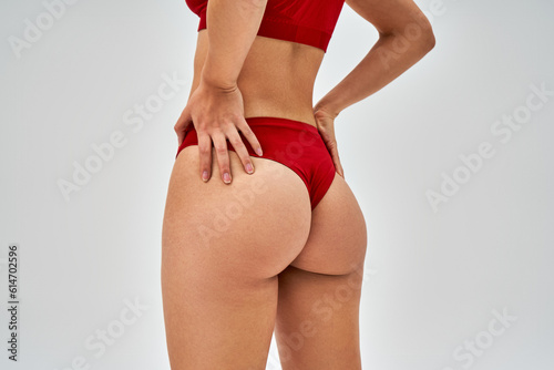 Cropped view of seductive woman in red bra and panties touching hips while standing and posing isolated on grey, self-acceptance and body positive concept