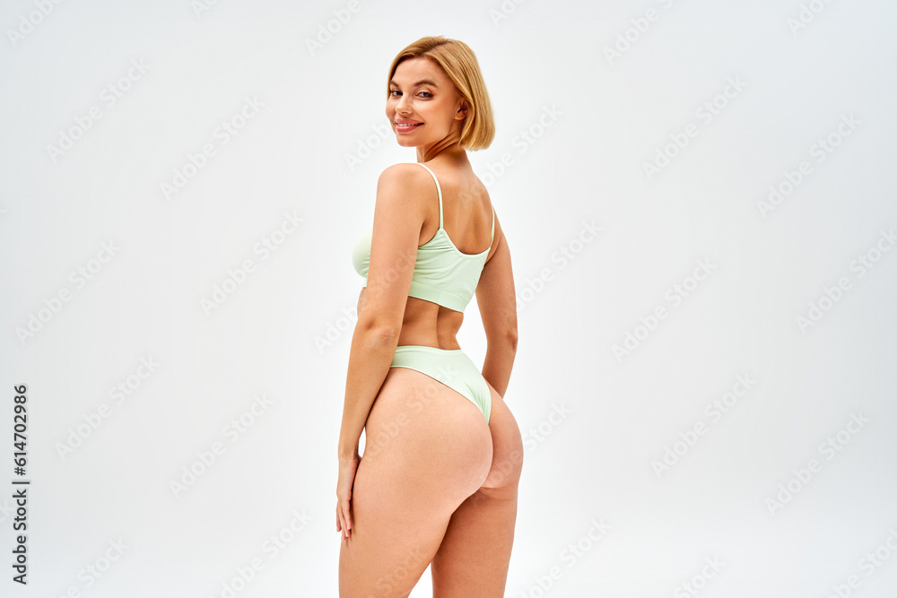 Cheerful young blonde woman in light green bra and sexy panties looking at  camera while posing isolated on grey, self-acceptance and body positive  concept, femininity Stock Photo
