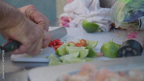 A chef slices a chilli with a sharp knife next to cut limes on a white chopping board. photo