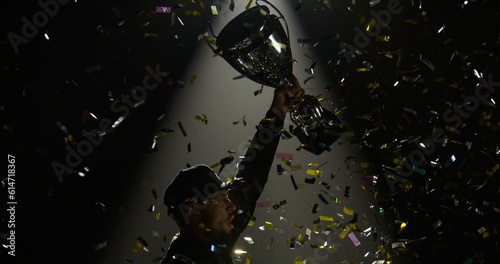 Silhouette of race car driver celebrating the win in a race against bright stadium lights, rising a trophy over his head