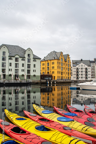 Kayaks docked in Brosundet, Ålesund, Norway. Beautiful Jugend buildings in the background reflected in calm sea. Vertical picture.	

