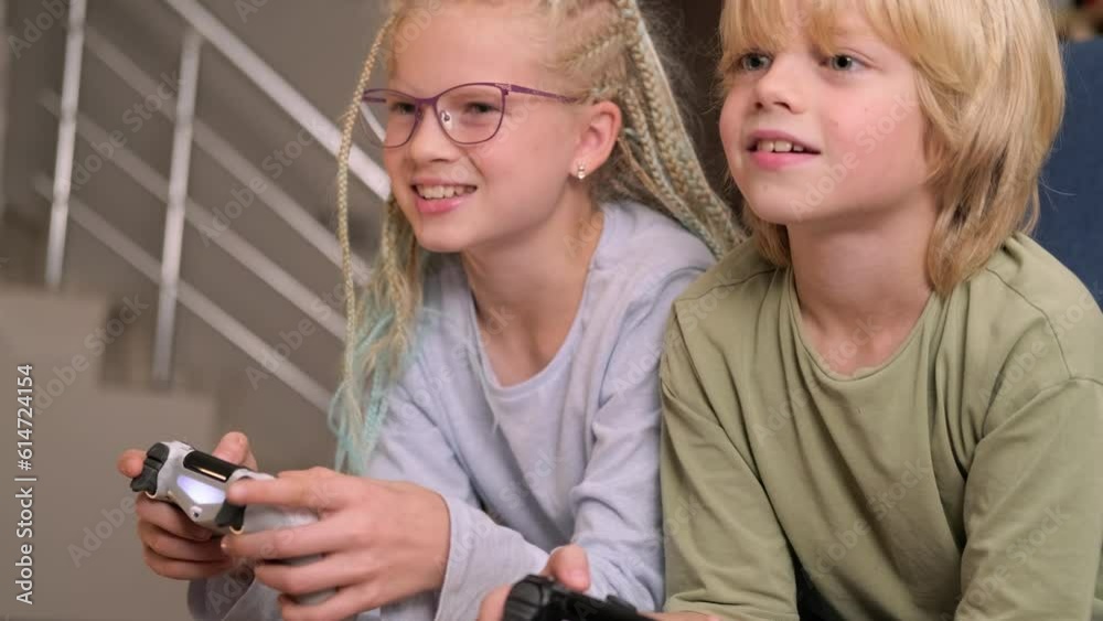 boy and girl playing video game console using joystick or controller while sitting at home, Two children small caucasian brother and sister happy children siblings, real people family leisure concept.