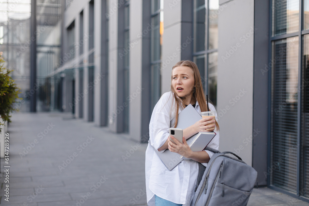 Hurry stressed blonde woman in white shirt outside a business center looking anxious as things slip from her hands. She juggles a phone, take away late and book. Bewildered looking girl, confused. Hurry stressed blonde woman in white shirt outside a business center looking anxious as things slip from her hands. She juggles a phone, take away late and book. Bewildered looking girl, confused.