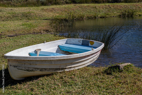 A small white colored wooden row boat on the green grass next to a lake