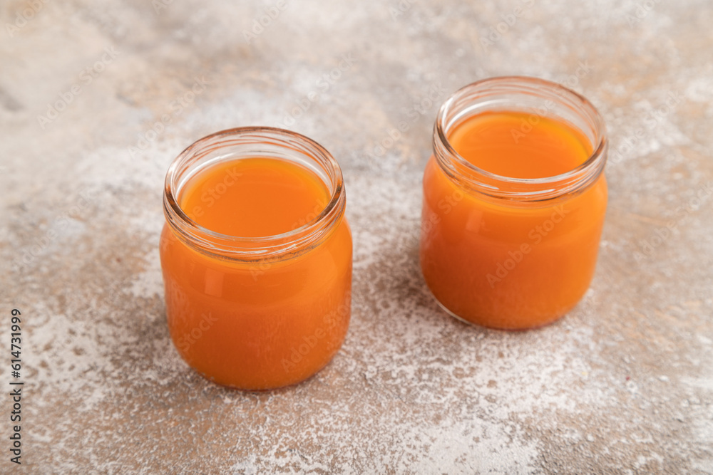 Baby puree with pumpkin, persimmon, mango in glass jar on brown concrete, side view Baby puree with pumpkin, persimmon, mango in glass jar on brown concrete, side view