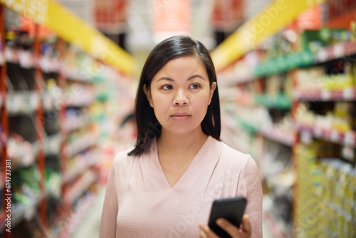 Woman looking at prices during inflation while doing shopping in supermarket