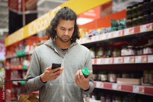 Man in supermarket comparing prices during inflation on cell phone photo