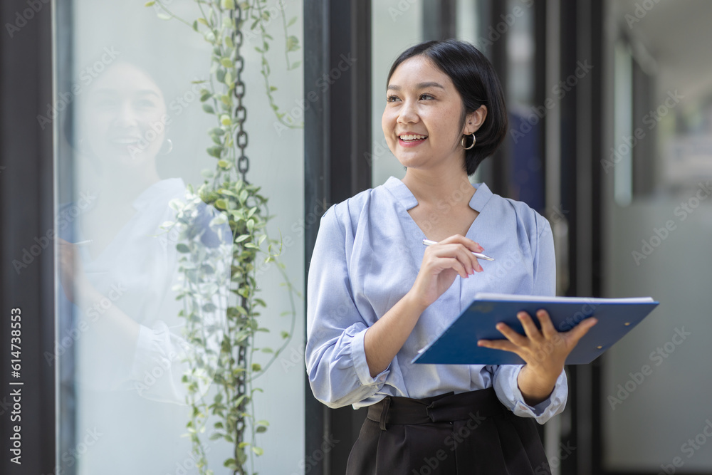 Boring young business Asian woman holding document file and looking at camera stand on a workplace office. Boring young business Asian woman holding document file and looking at camera stand on a workplace office.