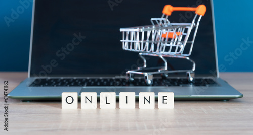 Online shopping concept. Shopping cart or trolley and laptop on wooden table.