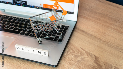 Online shopping concept. Shopping cart or trolley and laptop on wooden table.