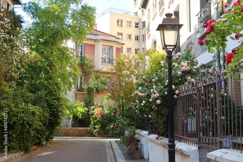 Ruelle pittoresque dans la Cité Florale, dans la ville de Paris, ensemble de rues végétalisées avec de nombreuses fleurs, arbres et plantes vertes dans de petits jardins devant les maisons (France)