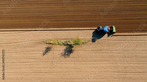 Aerial view of a tractor plowing a field around a small tree and flower strip seen directly from above, Germany