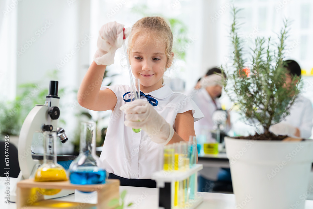 Caucasian cute girl wearing lab coat using dropper and transfer solution into test tube to mix it together in the elementary classroom. Learning chemistry and do the experiment in the school Caucasian cute girl wearing lab coat using dropper and transfer solution into test tube to mix it together in the elementary classroom. Learning chemistry and do the experiment in the school