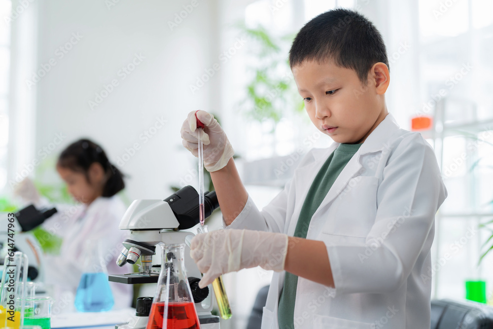 Asia cute boy wearing lab coat using dropper and transfer solution into test tube to mix it together in the elementary classroom. Learning chemistry and do the experiment in the school Asia cute boy wearing lab coat using dropper and transfer solution into test tube to mix it together in the elementary classroom. Learning chemistry and do the experiment in the school