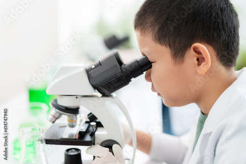 Close up of Young Asia scientist boy wearing lab coat and using microscope to see the structure of leaf In the laboratory at school. Chemistry experiment in the elementary school