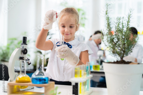 Caucasian cute girl wearing lab coat using dropper and transfer solution into test tube to mix it together in the elementary classroom. Learning chemistry and do the experiment in the school