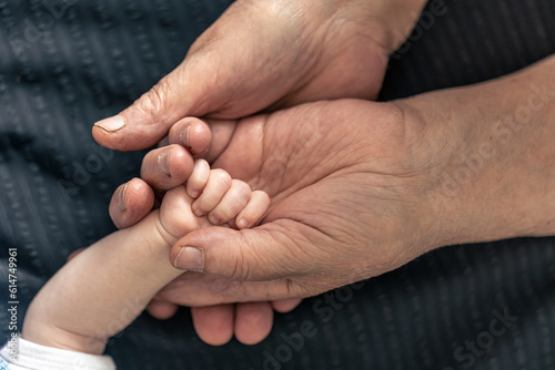 The handle of a newborn in the hands of a grandmother, close-up.