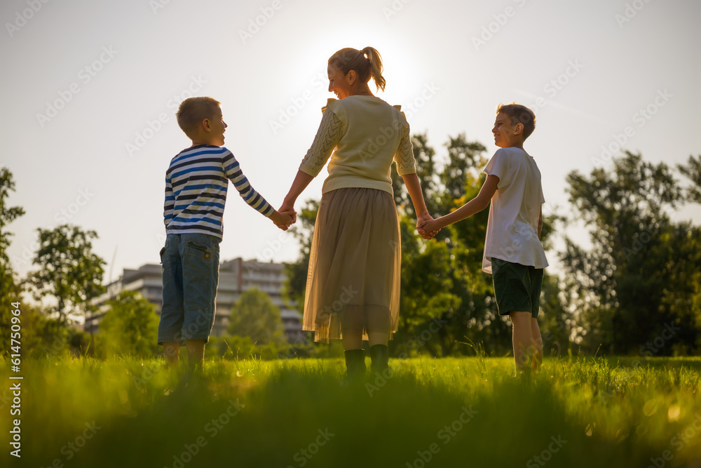 Happy mother is playing with her sons in park. They are holding hands and enjoying sunset. Happy mother is playing with her sons in park. They are holding hands and enjoying sunset.