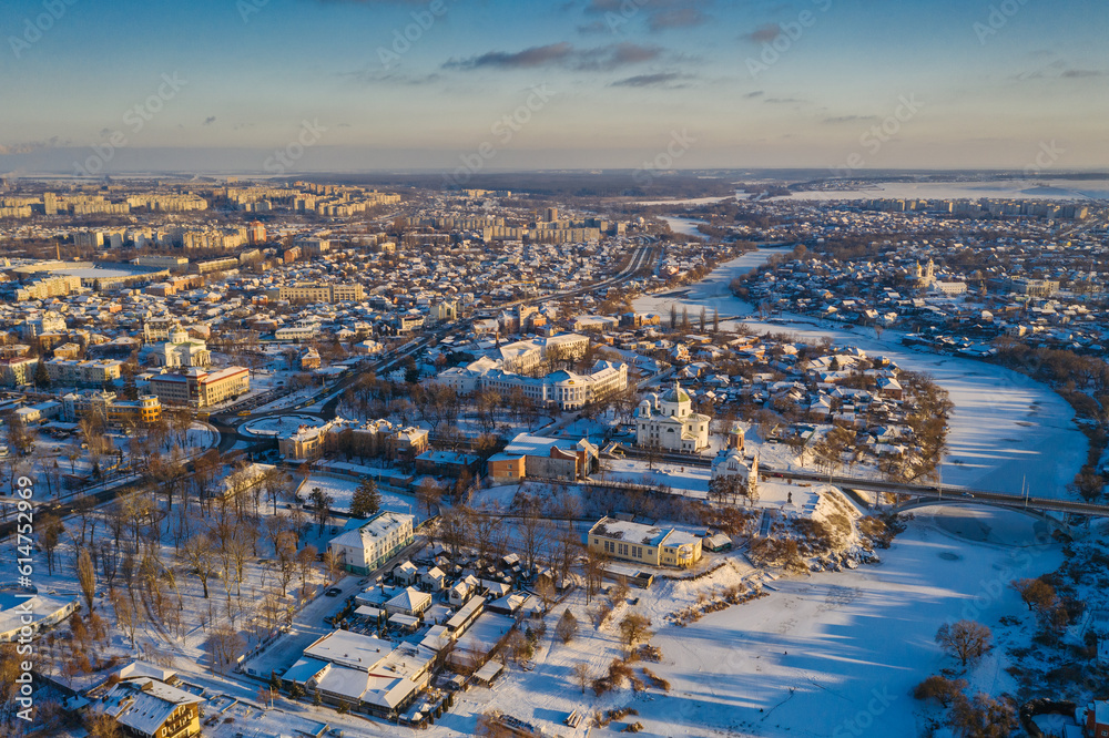 Nice top view of the winter city. Houses and buildings in the snow. Bridge over river. Orthodox churches and a Catholic cathedral. The river is covered with ice.