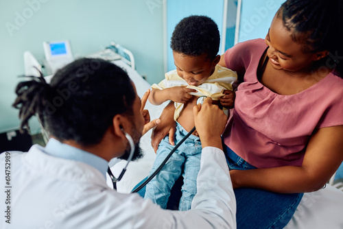 Black pediatrician examining kid with stethoscope during medical appointment at doctor's office. photo