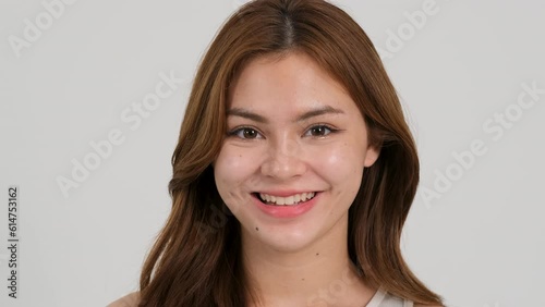 Close-up beauty portrait of young woman with smooth healthy skin, she gently touches her face with her fingers on light grey background and smiles. Skincare concept