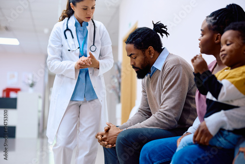Distraught black man and his family communicating with female doctor in waiting room at clinic.