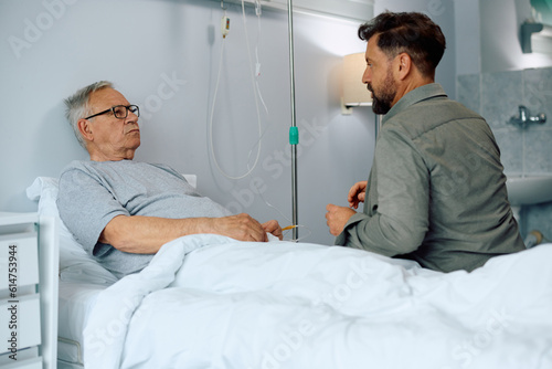 Senior man talks to his son who came to visit him in hospital.