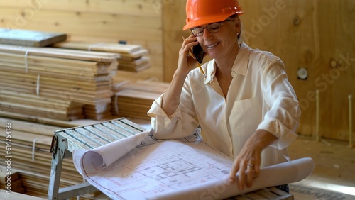 Front shot of woman architect on phone discussing and reviewing blueprints on a new construction job site. photo