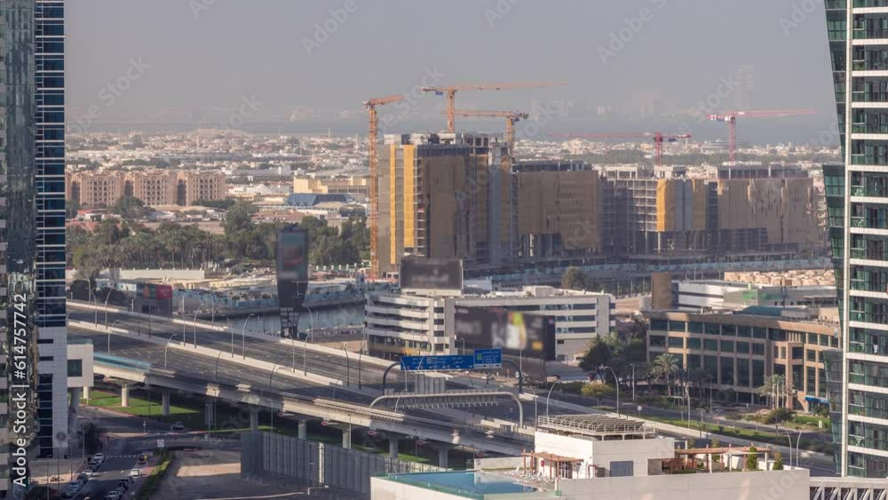 Construction site around Dubai water canal with many cranes aerial timelapse. Houses and villas are behind. Traffic on the highway bridge at morning with long shadows Construction site around Dubai water canal with many cranes aerial timelapse. Houses and villas are behind. Traffic on the highway bridge at morning with long shadows