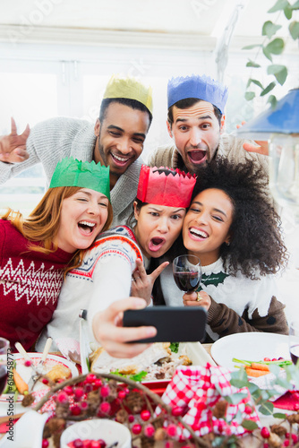 Silly friends in paper crowns taking selfie at Christmas dinner