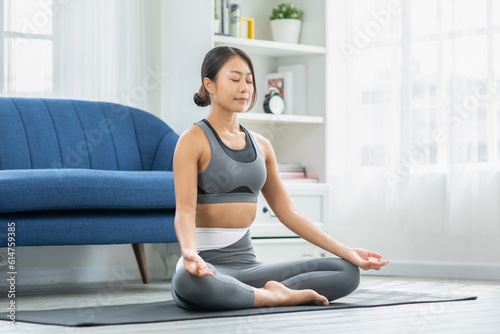 Calm of wellness Asian young woman sit on carpet breathing with yoga lotus pose,Yoga meditation of young healthy woman relax and comfortable at white cozy home,Yoga Exercise for Wellness Concept