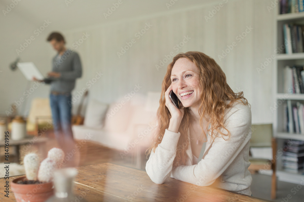 Fototapeta premium Smiling woman talking on cell phone at dining table
