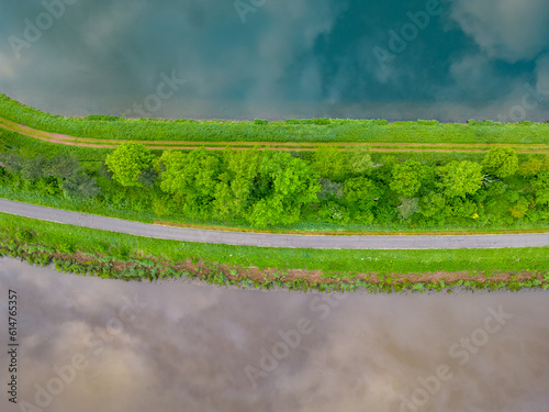 Top view or aerial view of a canal and a river next to eachother through a sunny rural landscape in spring, with a landslide with green, tree and dirt roads in between. High quality photo photo