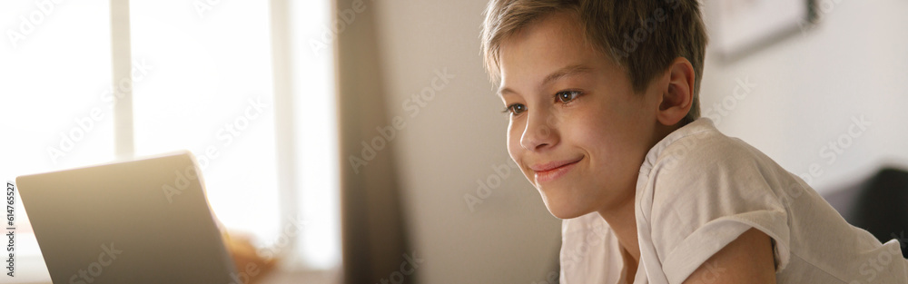 Young boy lies on the bed and looks into an open laptop. Home education concept Young boy lies on the bed and looks into an open laptop. Home education concept