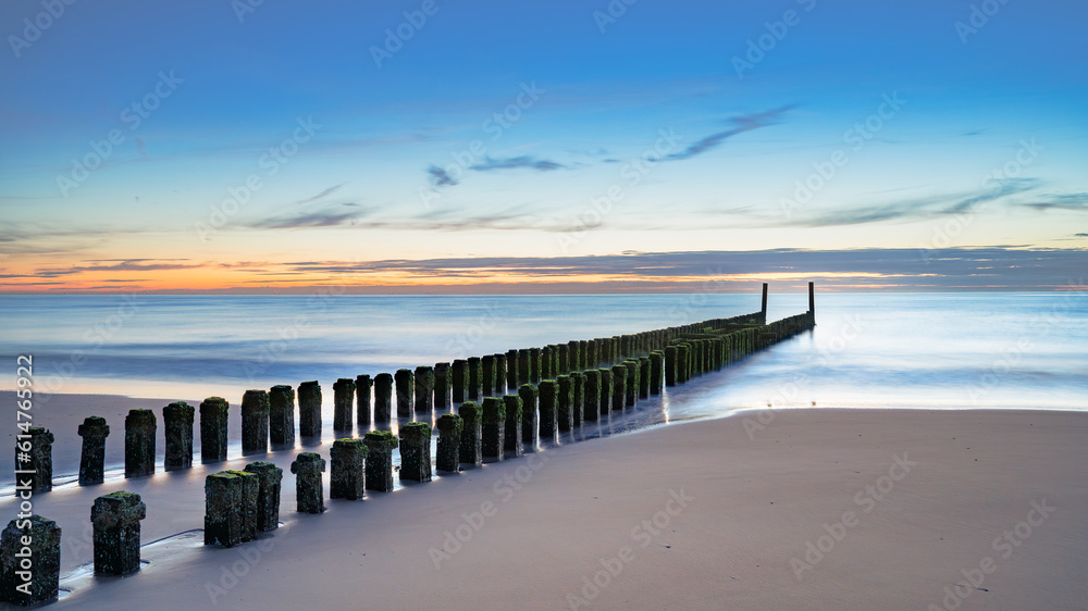 Weathered wooden posts on Dutch beach in winter. It is low tide now.