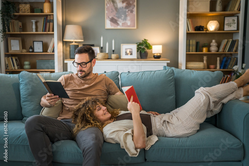 Fototapeta man and woman caucasian adult couple read books at home on sofa bed