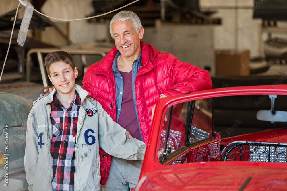 Portrait smiling father son next to classic car in auto repair shop - obrazy, fototapety, plakaty 