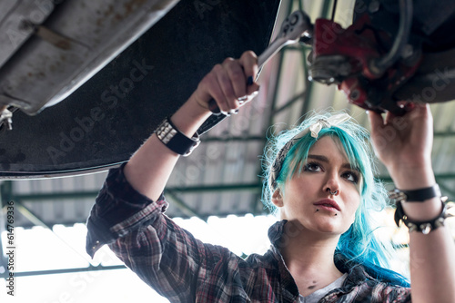 Young female mechanic with blue hair fixing car in auto repair shop