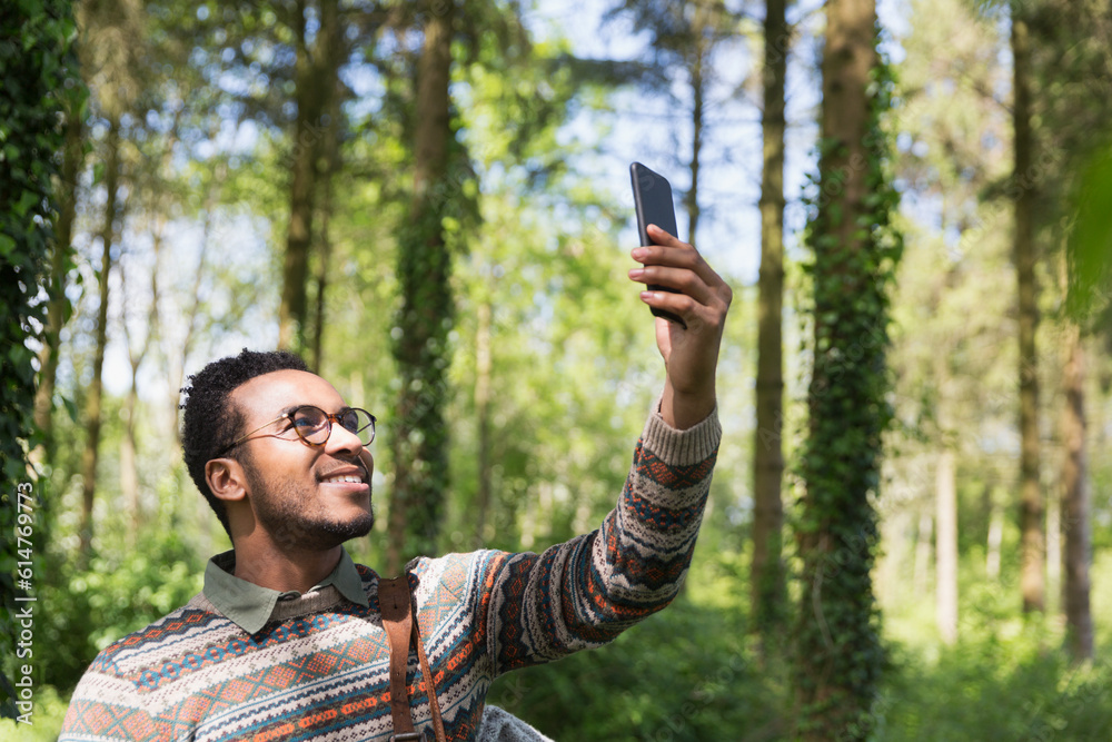 Smiling man taking selfie with camera phone in sunny woods Smiling man taking selfie with camera phone in sunny woods